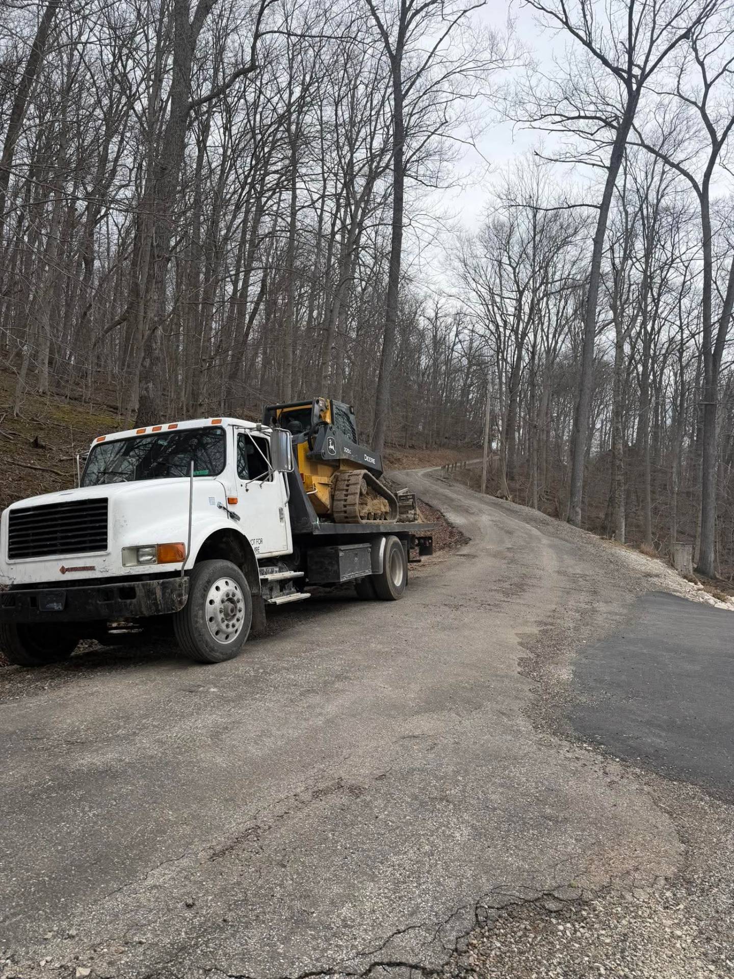 Equipment hauling on flatbed truck with tracked skid steer in Ohio hills